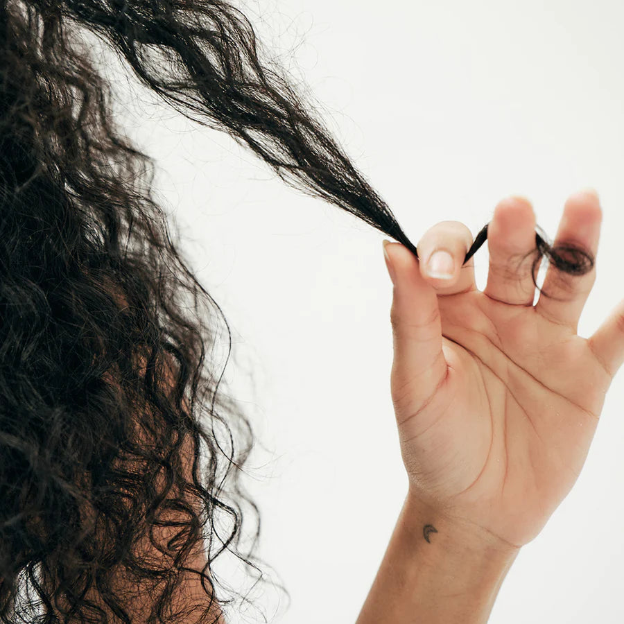 This shows a model with curly hair twisting a piece of hair in her hands. She is applying the hair serum. The serum is meant to moisturize your hair and help with breakage and heat protection. 